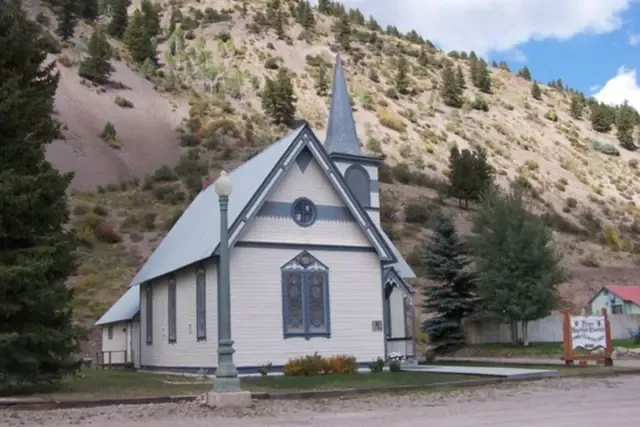 The historic white Baptist church in Lake City below a pine-dotted hillside