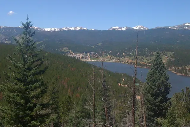 Small wooden mountain house among aspens and pines with high peaks behind in Nederland