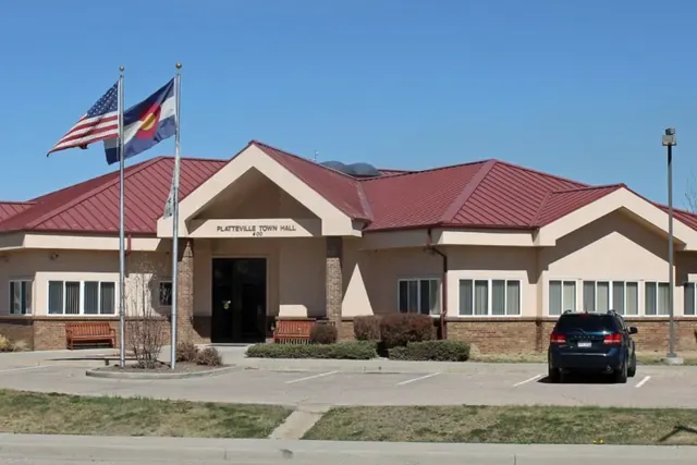 Platteville town hall with a red roof and flags on a clear day